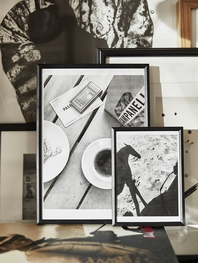 Black framed photos displayed on a table. One shows dishware, another horse silhouette. Modern, minimalist design.